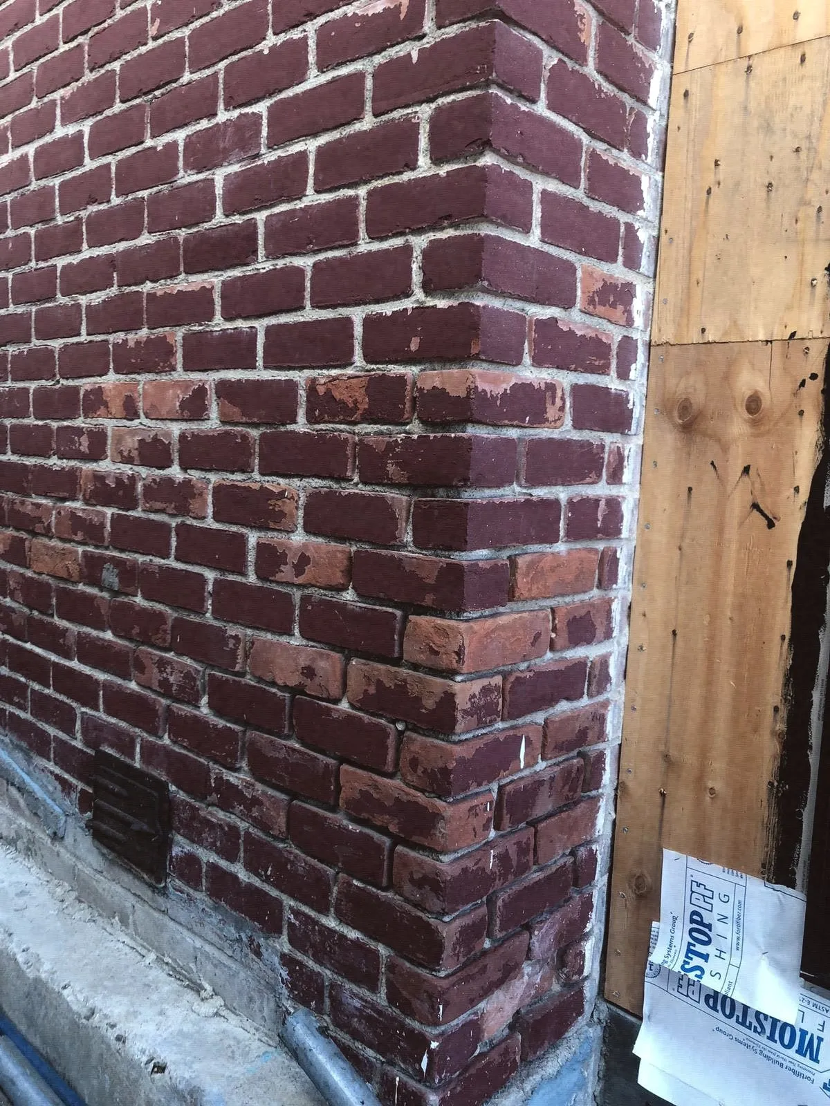 The corner of a brick chimney beside wood siding during repair
