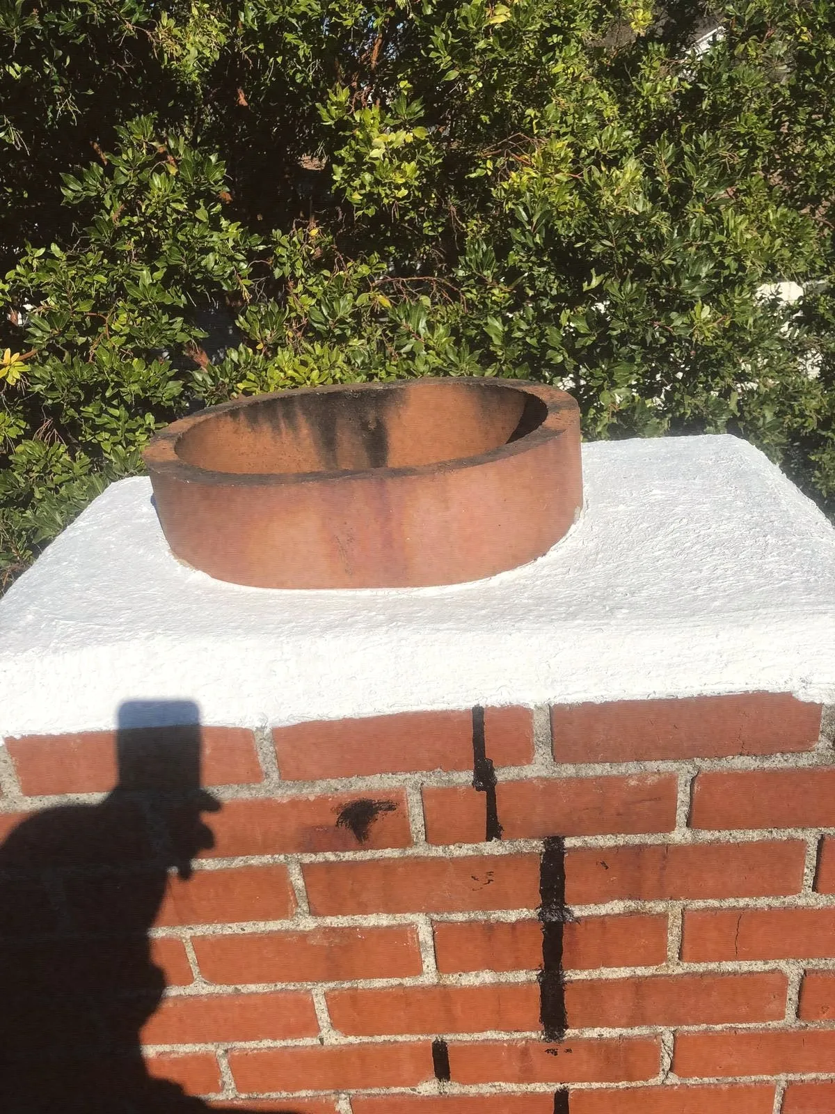 A terracotta clay flue tile with sooty streaks rising from a white crown on a brick stack