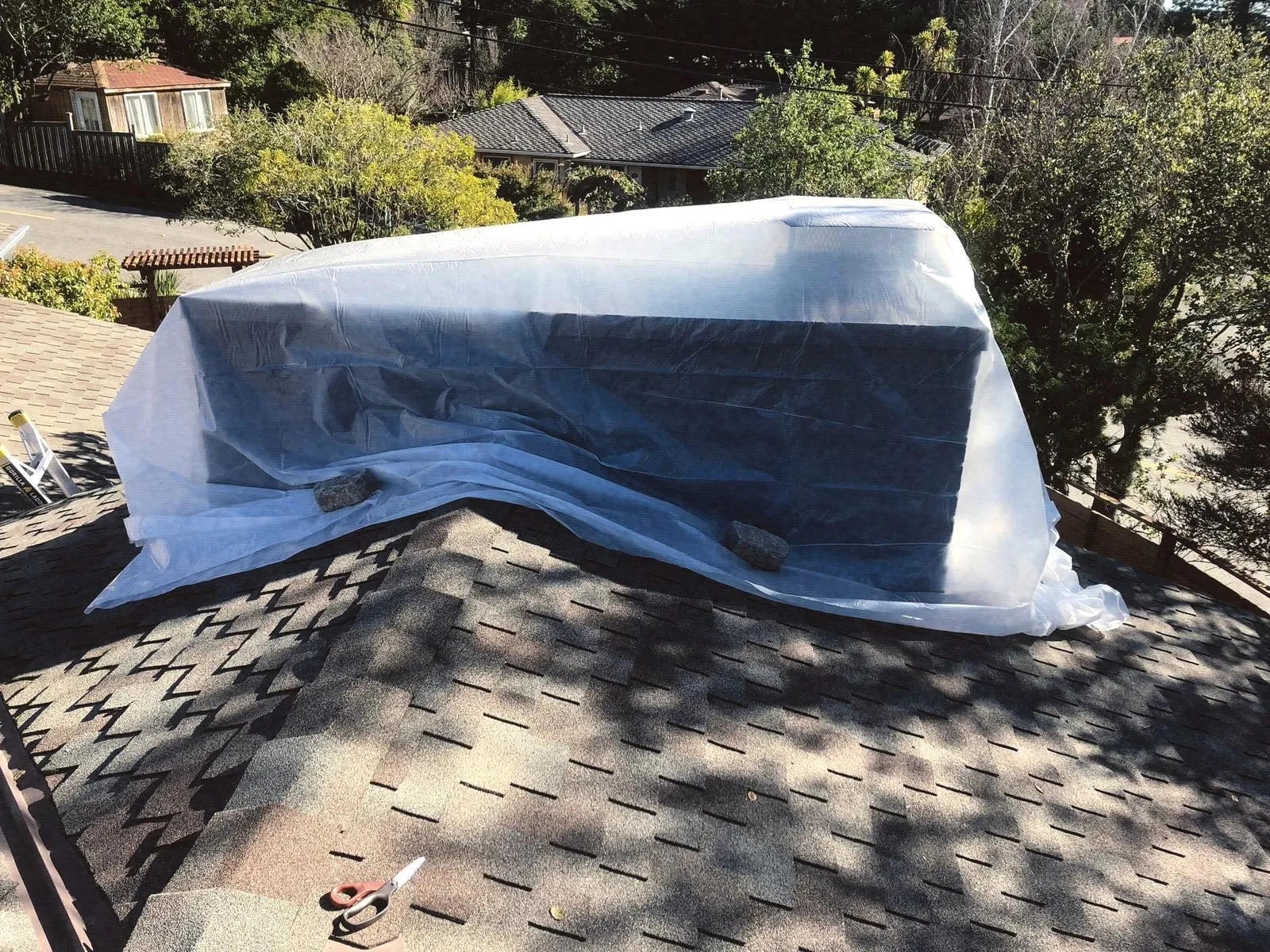 A chimney wrapped in protective plastic on a shingle roof during work