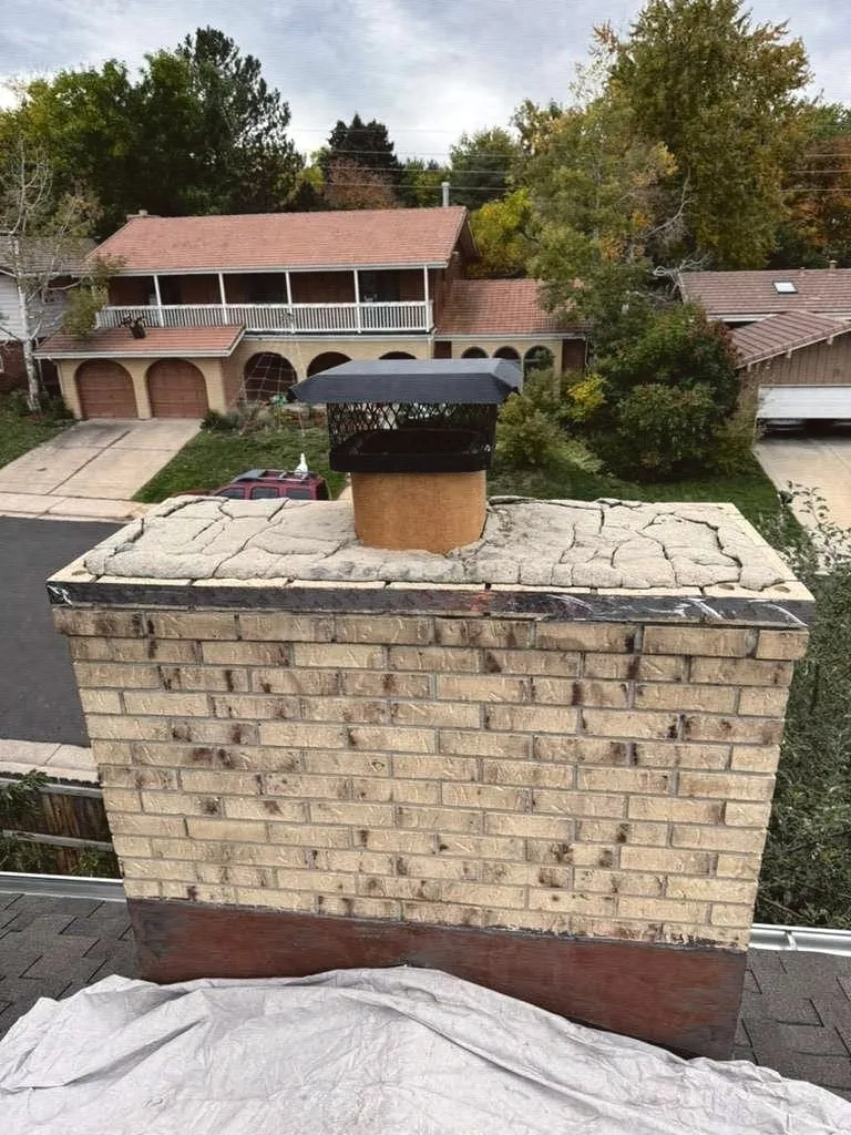 A tan brick chimney with a freshly formed concrete crown and a cap