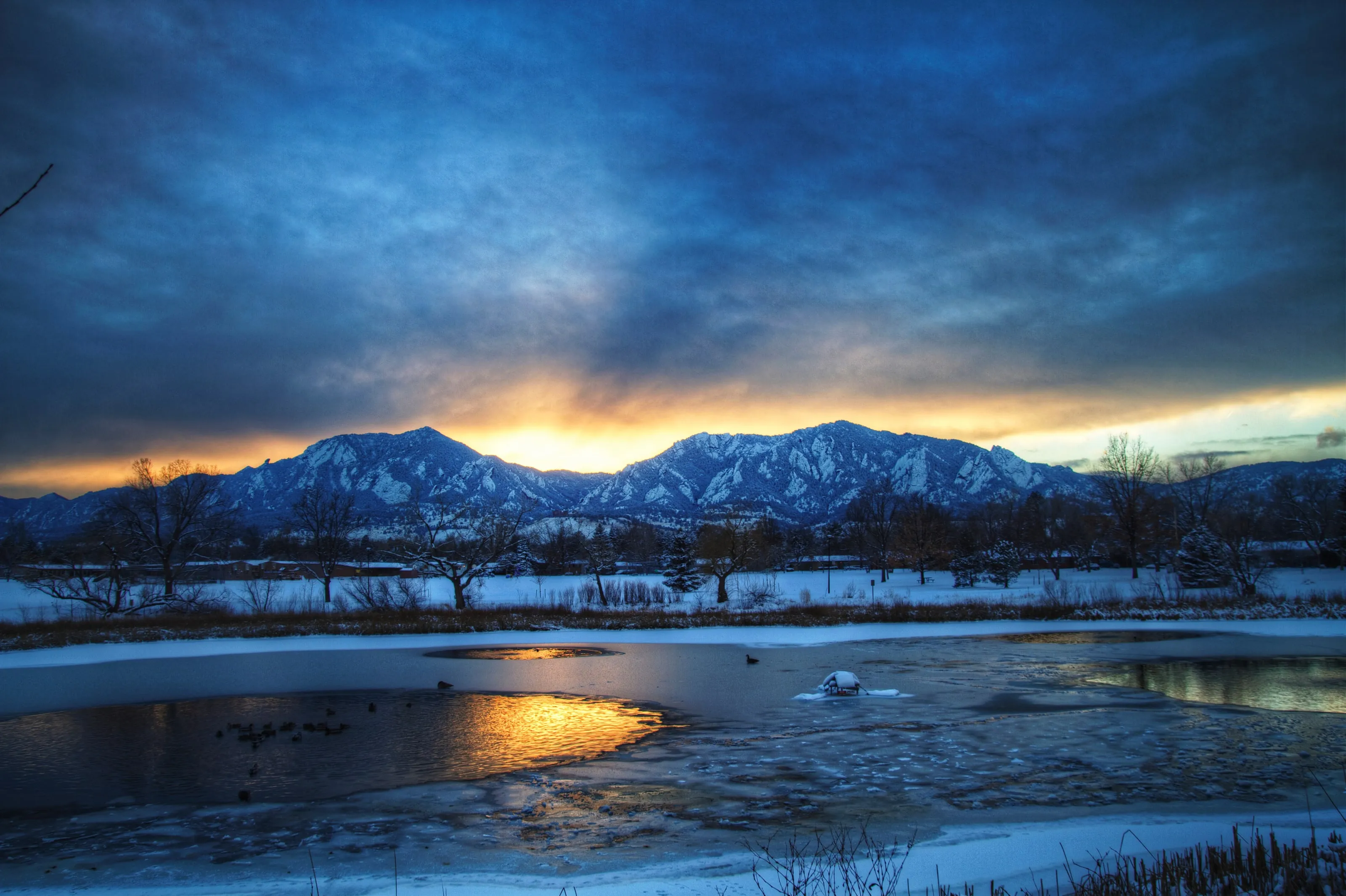Storm clouds over the Flatirons at dusk, with a frozen pond in the foreground